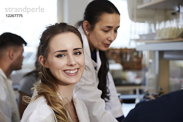 Porträt einer lächelnden jungen Schülerin  die im Chemielabor gegen Lehrerfreunde sitzt.