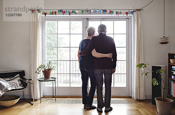 Durchgehende Rückansicht des Rentnerpaares mit Blick durchs Fenster zu Hause