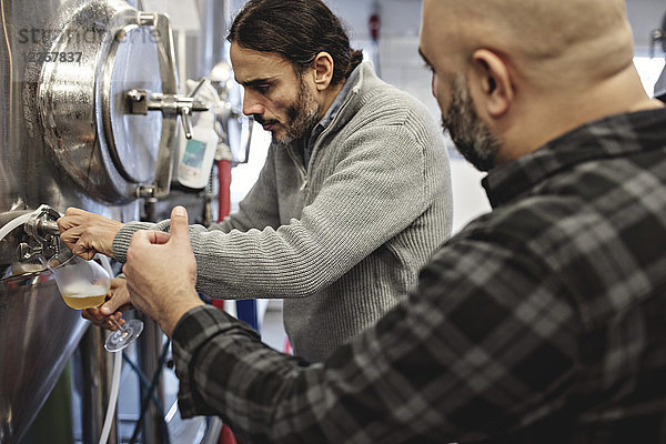 Mitarbeiter schaut auf den Mann  der Bier aus dem Vorratsbehälter in der Fabrik gießt.