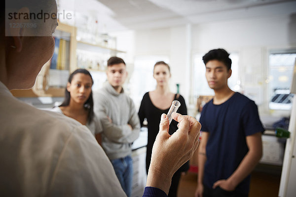 Rückansicht einer reifen Lehrerin mit Reagenzglas  die jungen multiethnischen Schülern im Labor erklärt.