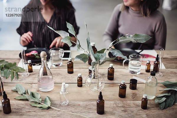 Mittelteil der jungen Kolleginnen am Tisch mit verschiedenen Parfümflaschen in der Werkstatt