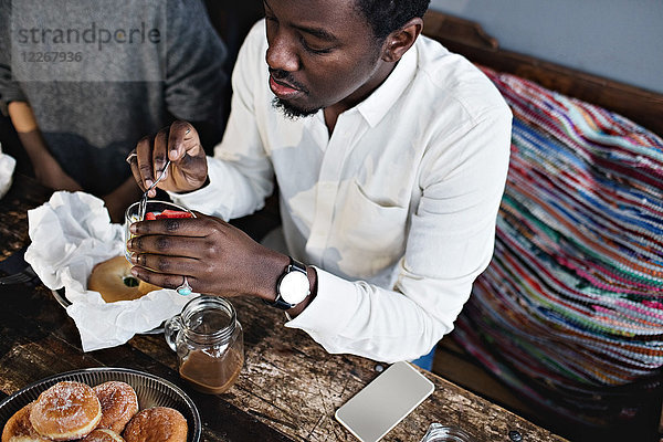 Hochwinkelansicht eines jungen Mannes beim Dessert am Holztisch im Restaurant