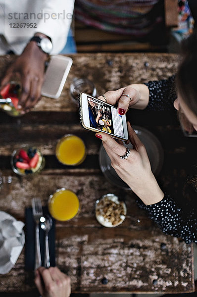 Hochwinkelansicht der Frau beim Fotografieren von Lebensmitteln über ein Smartphone am Tisch