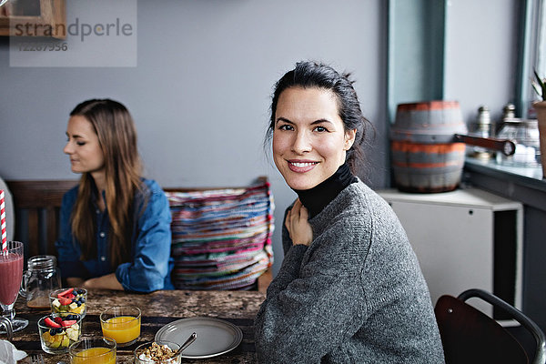 Porträt einer lächelnden Frau beim Brunch mit Freundin am Tisch