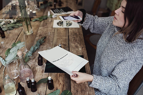 Hochwinkelaufnahme der mittleren erwachsenen Besitzerin beim Fotografieren am Tisch in der Werkstatt