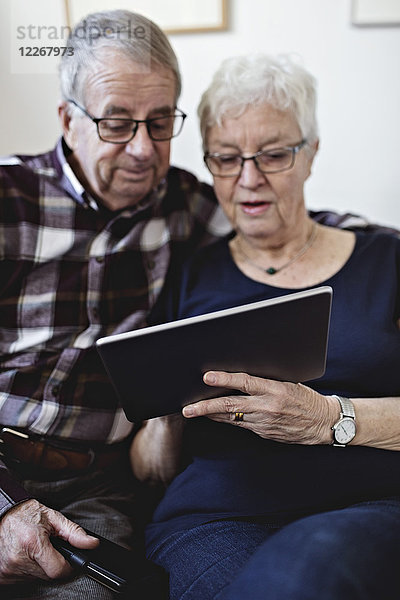 Seniorenpaar  das sich zu Hause ein digitales Tablett gegen die Wand teilt.