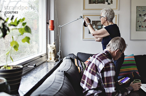 Seniorin mit Stehleuchte von Mann auf Sofa sitzend im Wohnzimmer zu Hause