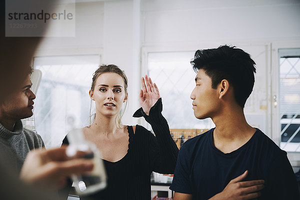 Junge Studentin steht mit erhobener Hand inmitten von Männern und schaut auf die Lehrerin im Chemielabor.
