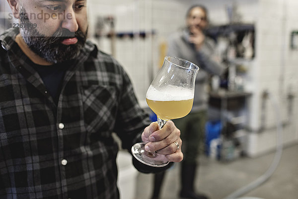 Zuversichtlicher Manager bei der Untersuchung von Bier im Glas mit Mitarbeiter im Hintergrund