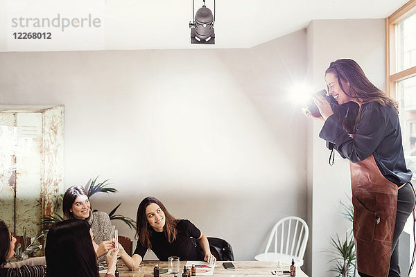 Fröhliche Frau beim Fotografieren weiblicher Kollegen am Tisch in der Werkstatt