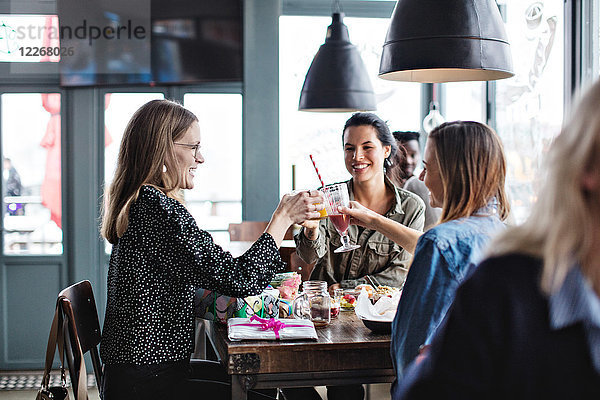 Lächelnde weibliche Freunde  die beim Sitzen am Esstisch im Restaurant anstoßen