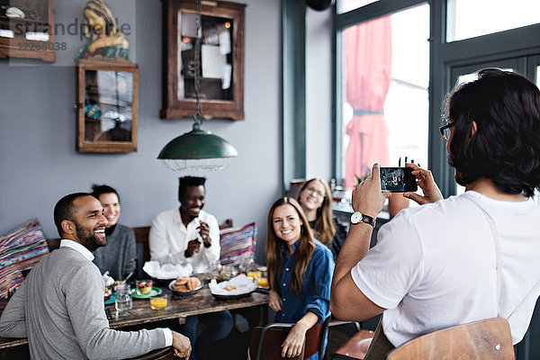Besitzer fotografiert lächelnde Freunde per Handy am Tisch im Restaurant