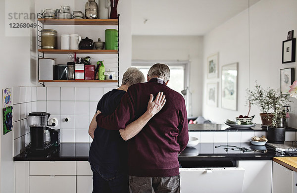 Rückansicht des pensionierten Seniorenpaares  das in der Küche zu Hause steht.