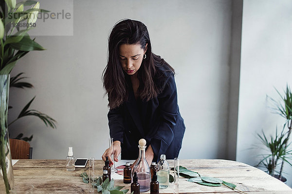 Mittlere erwachsene Unternehmerin bei der Zubereitung von Parfüm auf dem Tisch gegen die Wand im Workshop