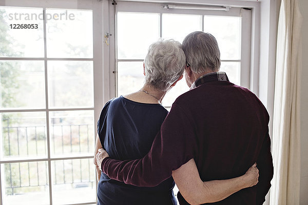 Rückansicht des Rentnerpaares beim Blick durchs Fenster zu Hause