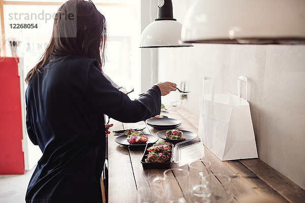 Frau beim Zubereiten des Essens auf dem Teller bei Tisch in der Werkstatt
