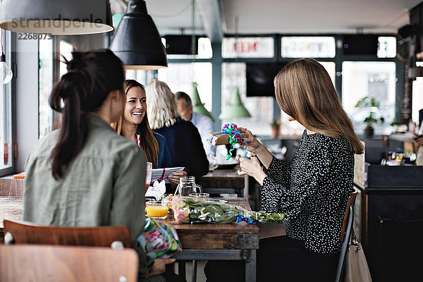 Lächelnde weibliche Freunde  die die Frau beim Sitzen am Esstisch im Restaurant ansehen.