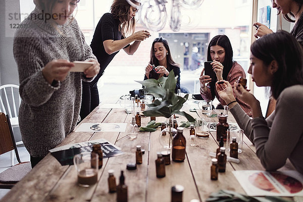 Multiethnische Mitarbeiterinnen beim Fotografieren von Parfums auf dem Tisch in der Werkstatt