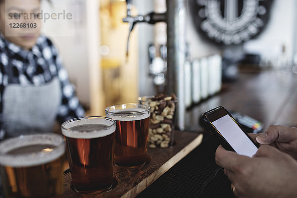 Kundin beim kontaktlosen Bezahlen per Smartphone an die Barkeeperin für Bier am Schalter