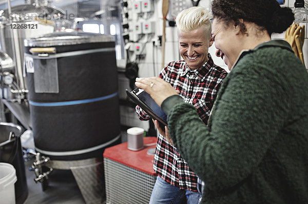 Lächelnde Arbeiterinnen diskutieren bei der Arbeit in der Brauerei über das digitale Tablett