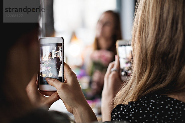 Frauen fotografieren Freund durch Smartphones am Esstisch im Restaurant
