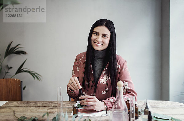 Porträt einer lächelnden Unternehmerin bei der Zubereitung von Parfüm am Tisch in der Werkstatt