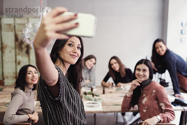 Lächelnde junge Frau nimmt Selfie mit weiblichen Mitarbeitern in der Werkstatt mit.