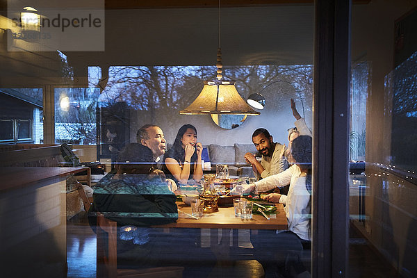 Mehrgenerationen-Familiengespräch beim Abendessen am Tisch durchs Fenster gesehen