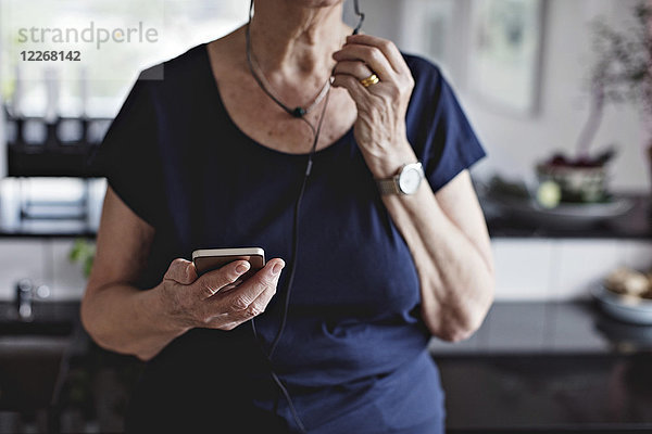 Mittelteil der älteren Frau mit Smartphone in der Küche zu Hause