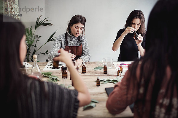 Multi-ethnische Kolleginnen bereiten Parfüm vor  während sie am Tisch in der Werkstatt sitzen.