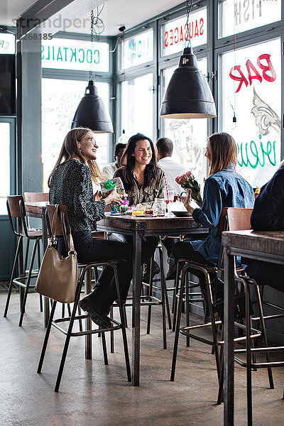 Volle Länge von lächelnden Freundinnen  die mit Geburtstagsgeschenken am Esstisch im Restaurant sitzen.