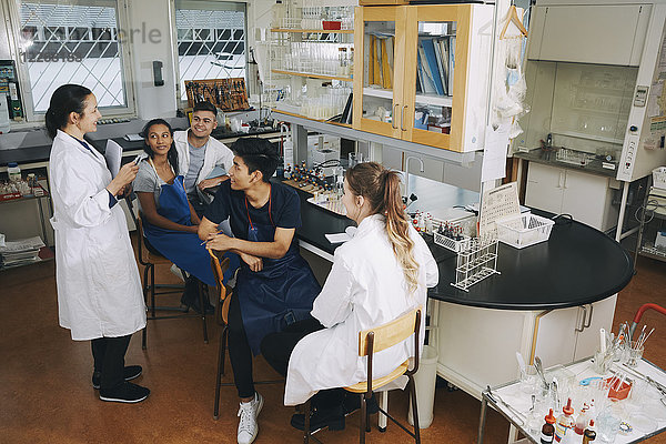 Volle Länge des reifen Lehrers  der jungen multiethnischen Universitätsstudenten im Chemielabor erklärt.