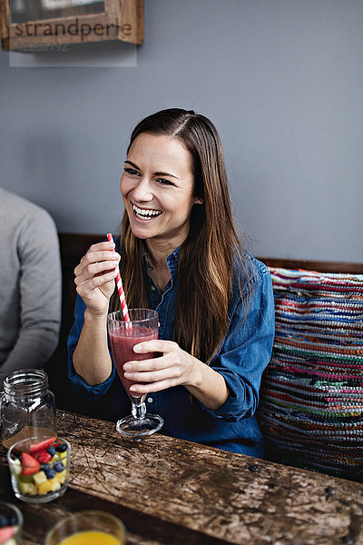 Lächelnde junge Frau beim Trinken am Tisch im Restaurant