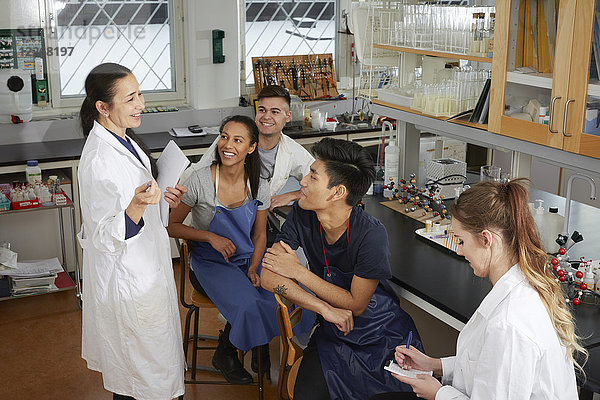 Fröhlicher  reifer Lehrer  der jungen multiethnischen Studenten  die im Chemielabor sitzen  erklärt.