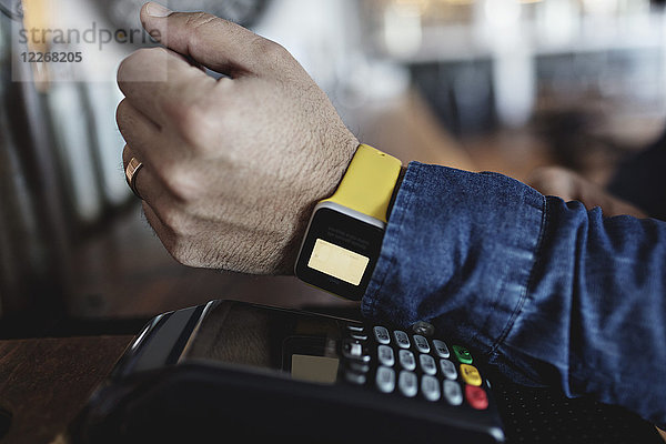 Abgeschnittenes Bild des Kunden beim kontaktlosen Bezahlen durch Smart Watch an der Theke