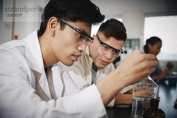 Junge männliche Studenten beim Mischen von Lösungen in Glaswaren im Chemielabor