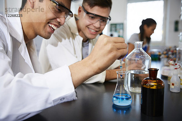 Lächelnde junge männliche Studenten beim Mischen von Lösungen in Glaswaren im Chemielabor