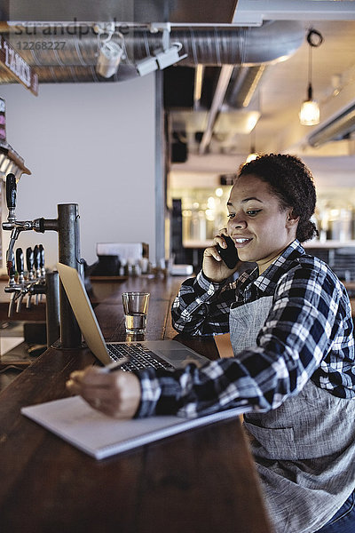 Lächelnde Managerin beim Telefonieren mit dem Laptop an der Theke