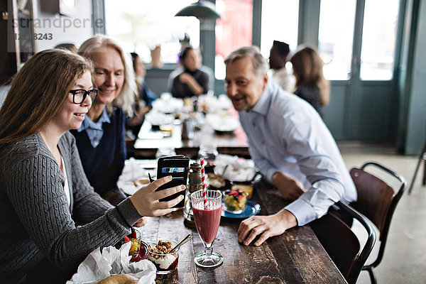 Lächelnde Tochter nimmt Selfie mit den Eltern mit  während sie am Tisch im Restaurant sitzt.