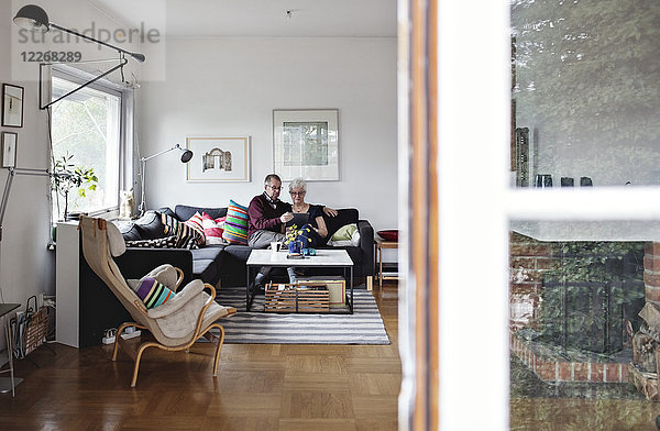 Seniorenpaar sitzt auf Sofa im Wohnzimmer zu Hause