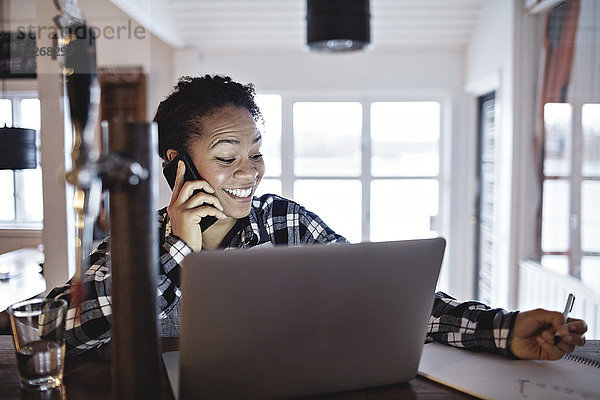 Fröhliche Managerin beim Telefonieren mit dem Laptop an der Theke