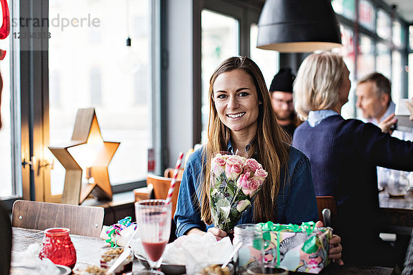 Porträt einer lächelnden Frau mit Geschenken am Esstisch im Restaurant