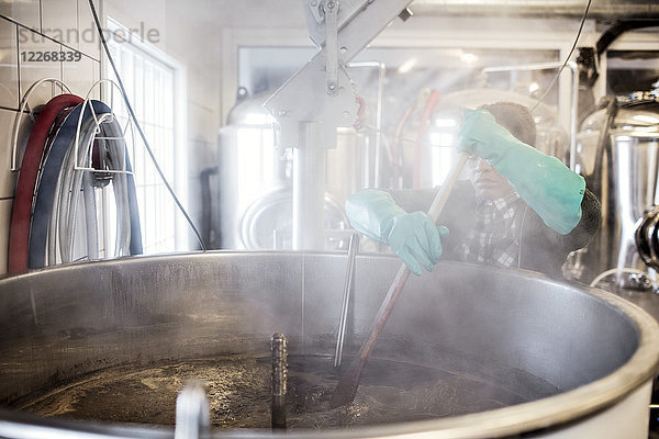 Arbeiter mit Handschuhen beim Rühren von Bier im Behälter in der Brauerei