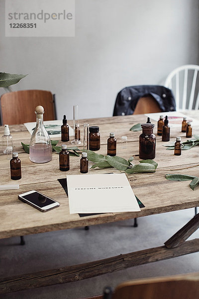 Hochwinkelansicht von Handy und Broschüre durch Parfümflaschen auf Holztisch in der Werkstatt