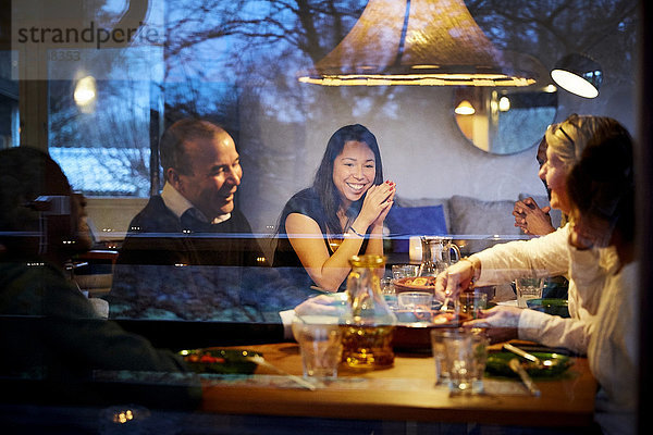 Mehrgenerationen-Familie genießt Abendessen am Tisch durch das Glasfenster gesehen