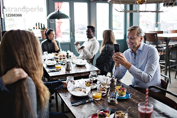 Man photographing women while friends sitting at table in restaurant
