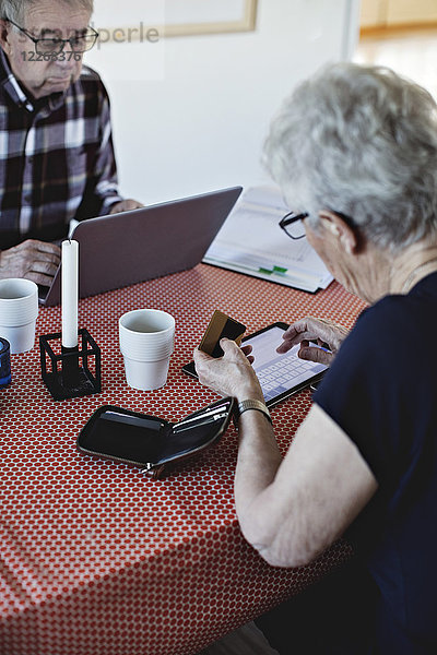 Seniorin mit Kreditkarte bei der Benutzung des digitalen Tabletts am Esstisch