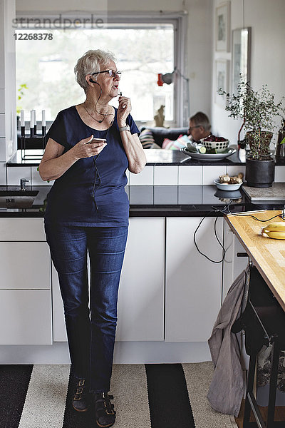 Volle Länge der älteren Frau stehend mit Smartphone in der Küche zu Hause
