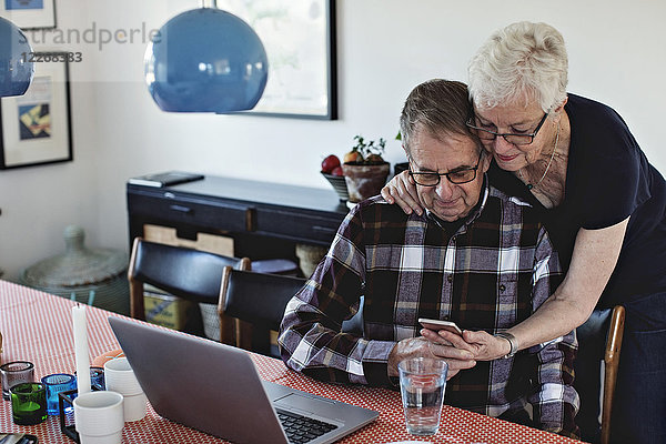 Senior Frau teilt Smartphone mit Mann am Esstisch