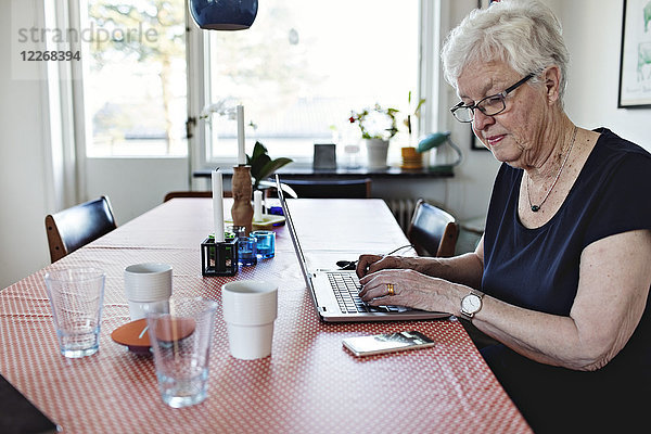 Seniorin mit Laptop beim Sitzen am Esstisch im Zimmer